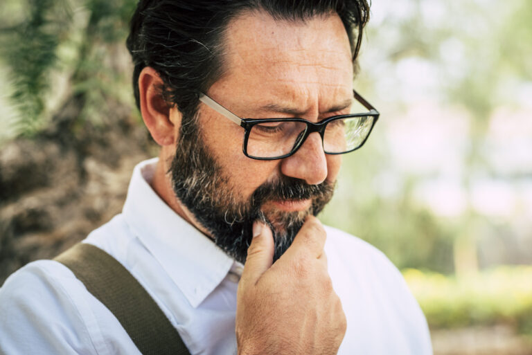 Worried man touching beard trying to figure out how to fix his cell phone.